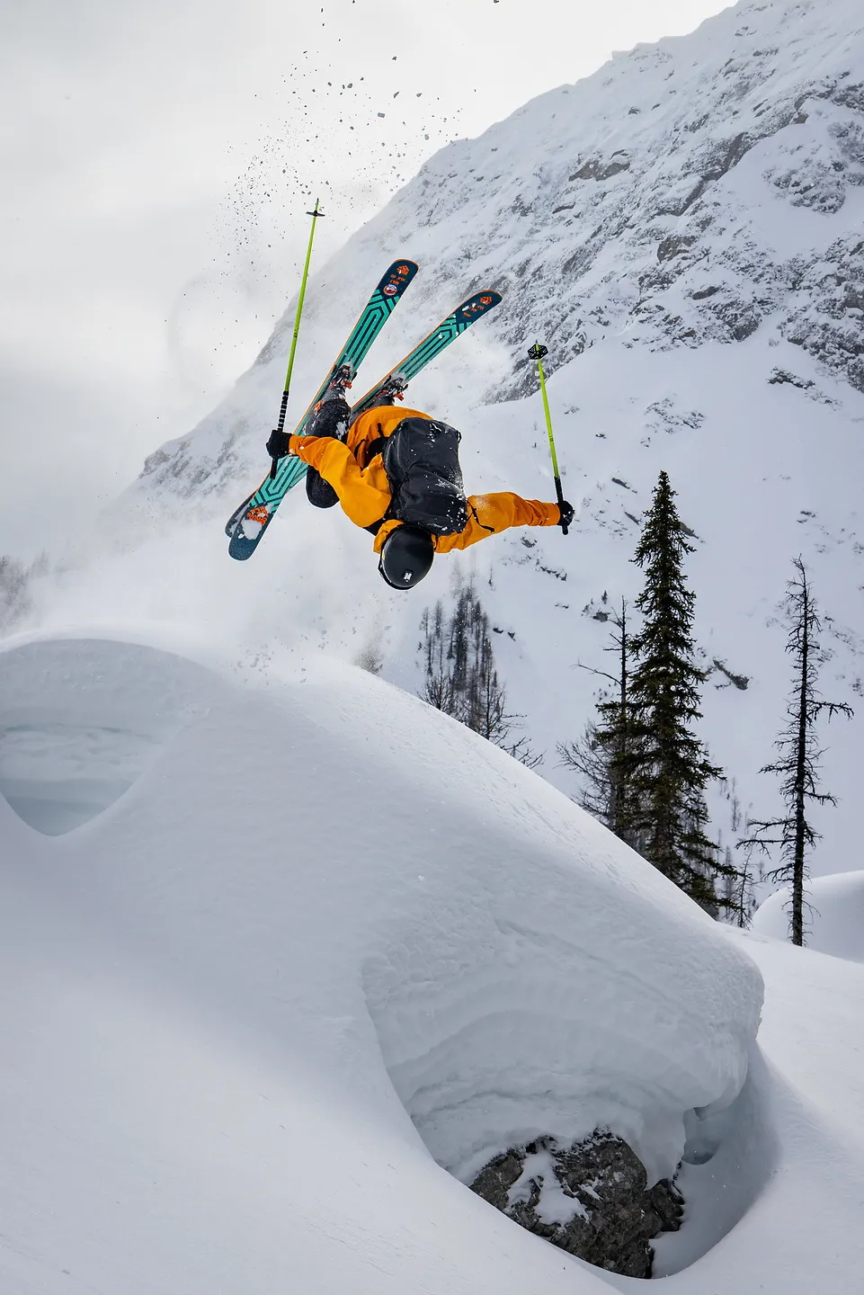 A skier in orange doing a backflip off a snow pillow