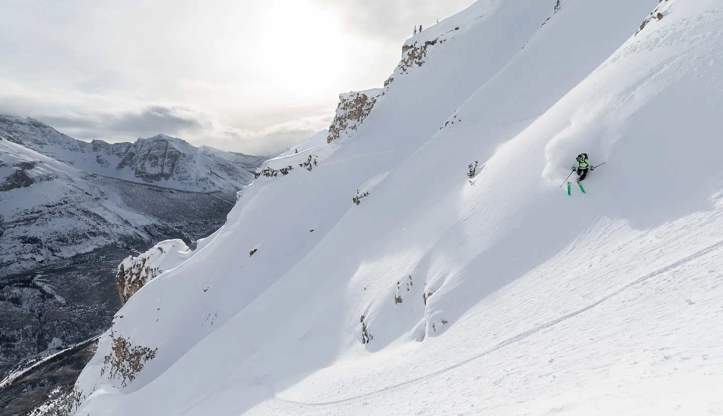 A skier on a steep sunlit face above a valley